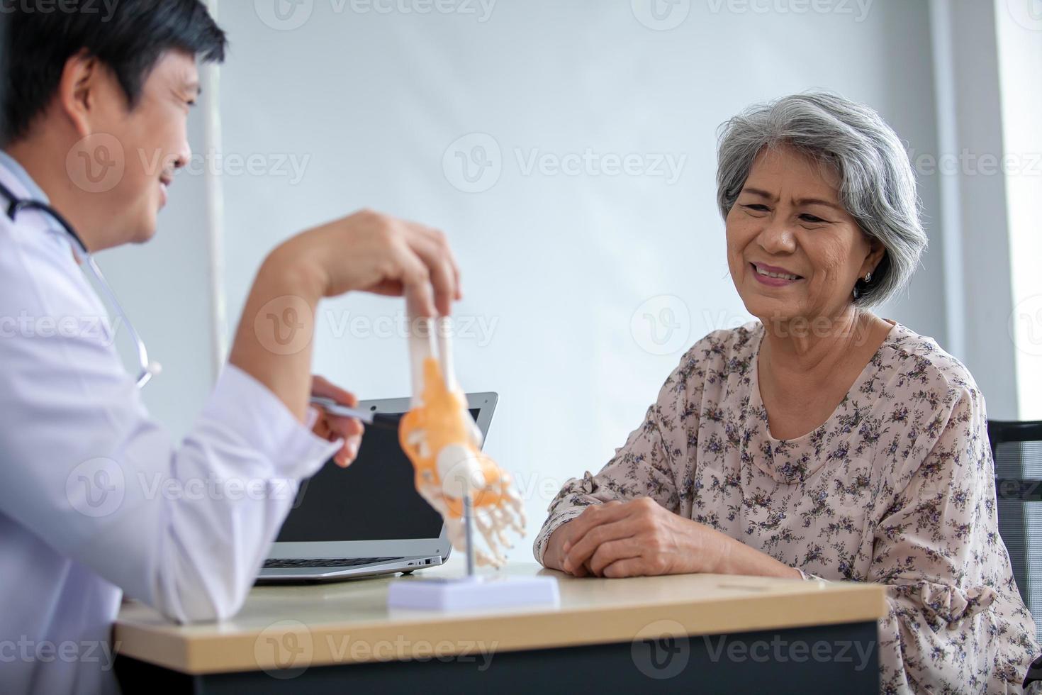 de dokter is uitleggen naar de senior geduldig de voet pijn met model. foto