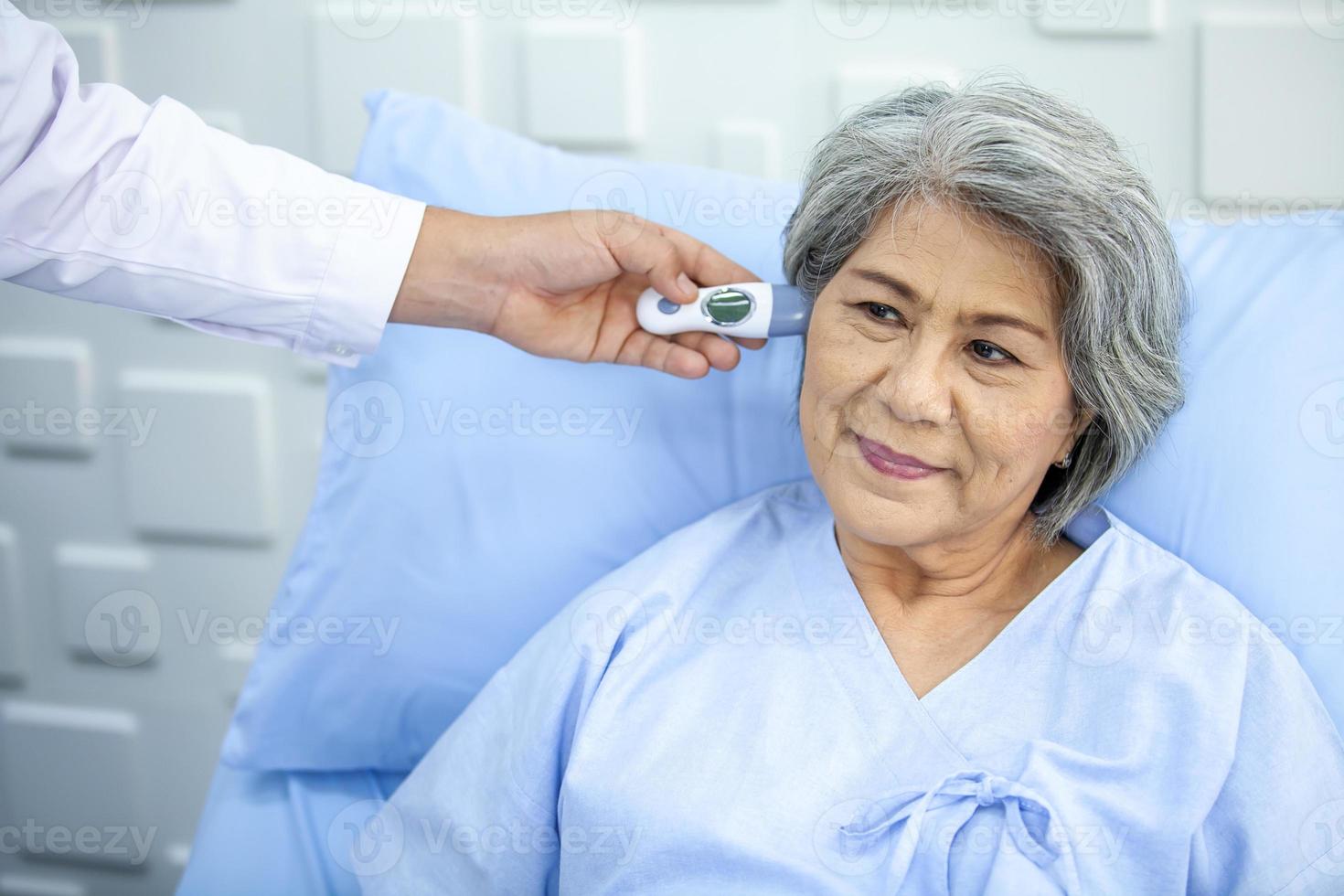 dokter is meten de temperatuur van senior geduldig Bij oor in de ziekenhuis, gezondheidszorg en geneeskunde concept. foto