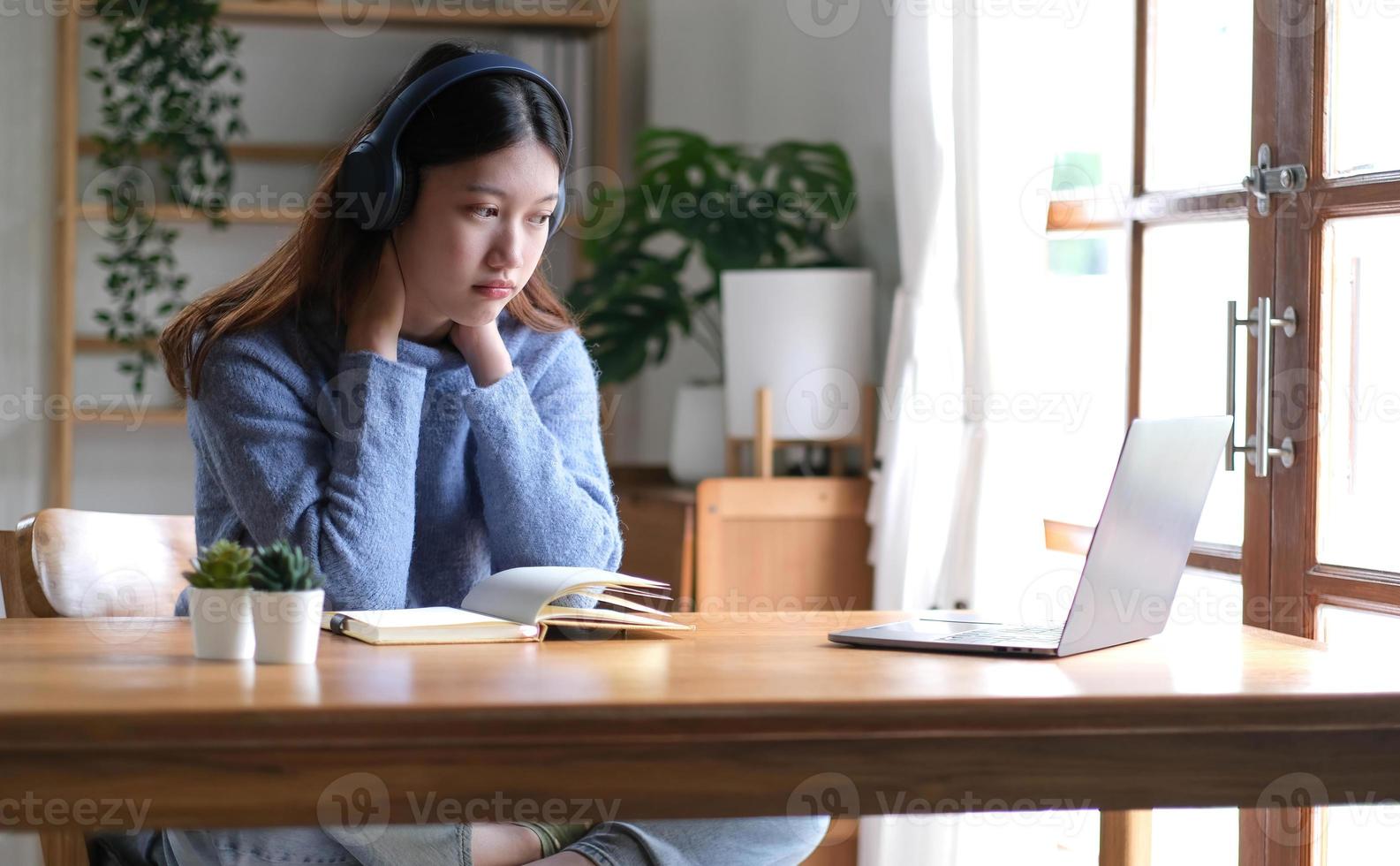 kant visie van Aziatisch zakenvrouw gebruik makend van computer werken online en browsen internet vervelend draadloze oortelefoons zittend in modern kantoor binnen. bedrijf carrière, internet en technologie foto