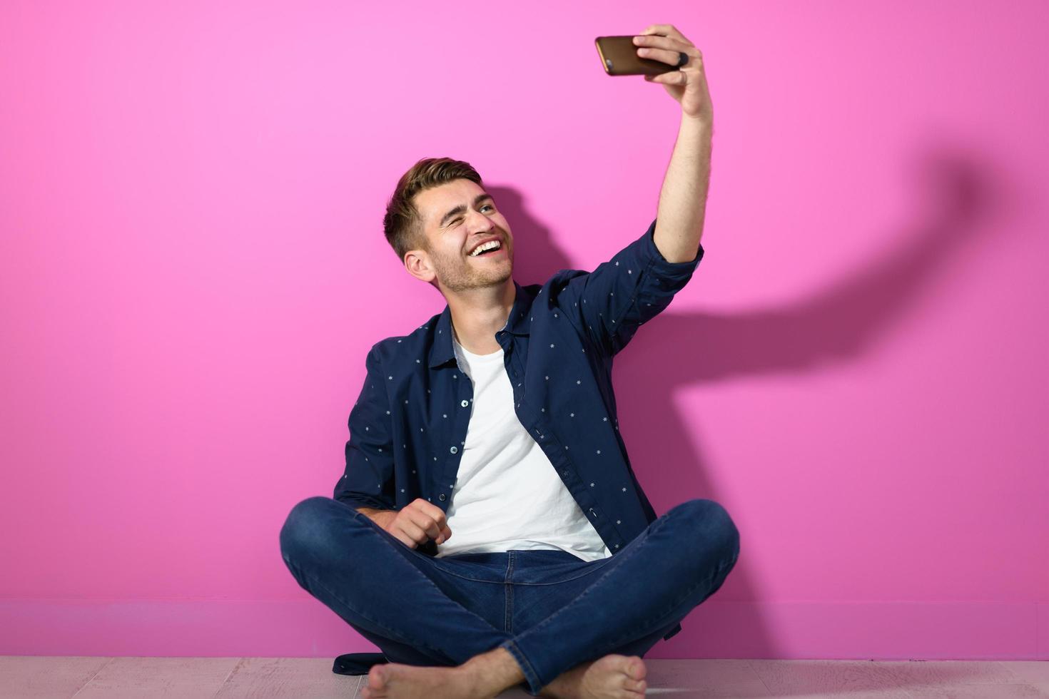 Mens zittend Aan de verdieping van de huis en gebruik makend van de telefoon foto