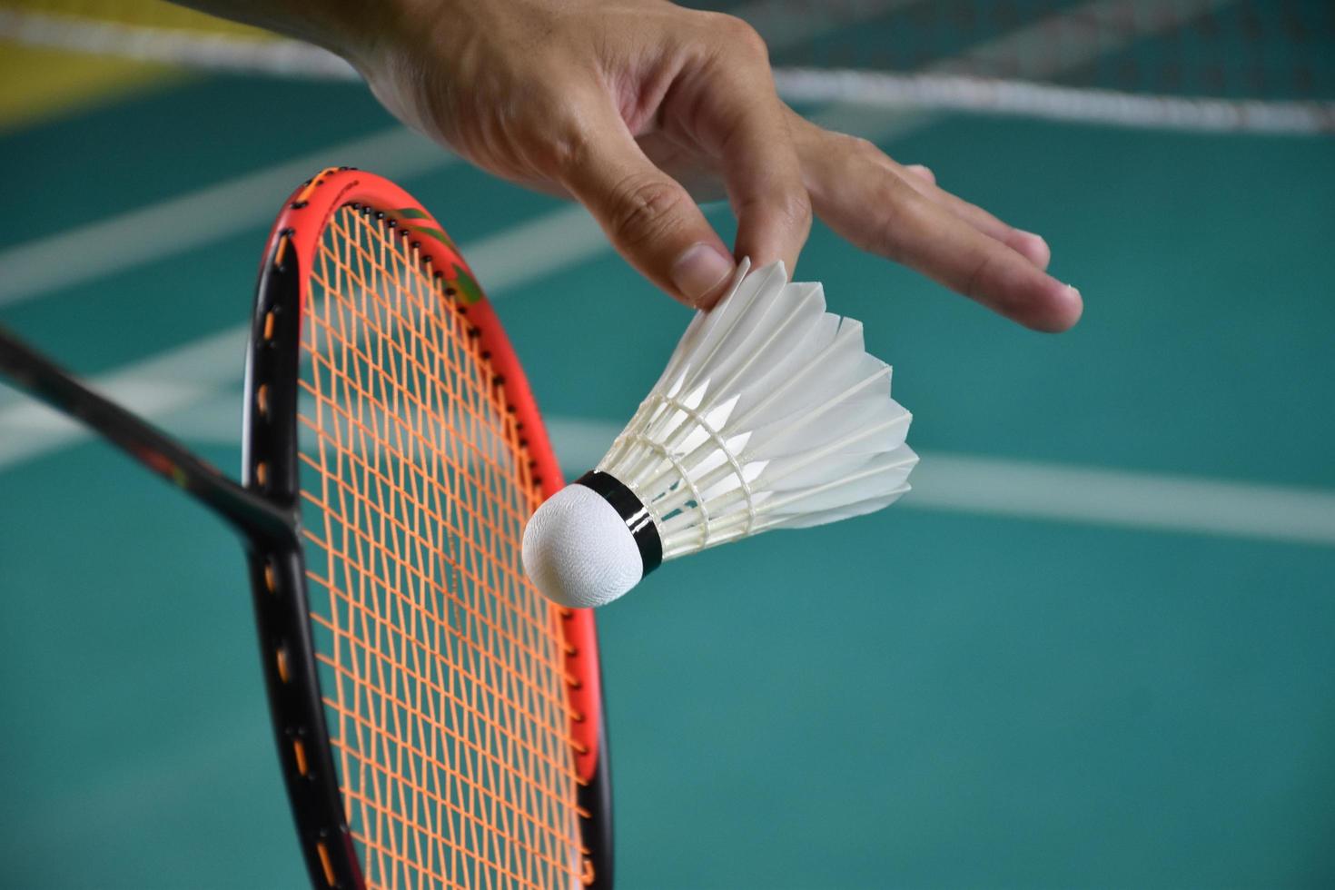 badminton speler houdt racket en wit room shuttle in voorkant van de netto voordat portie het naar een ander kant van de rechtbank. foto