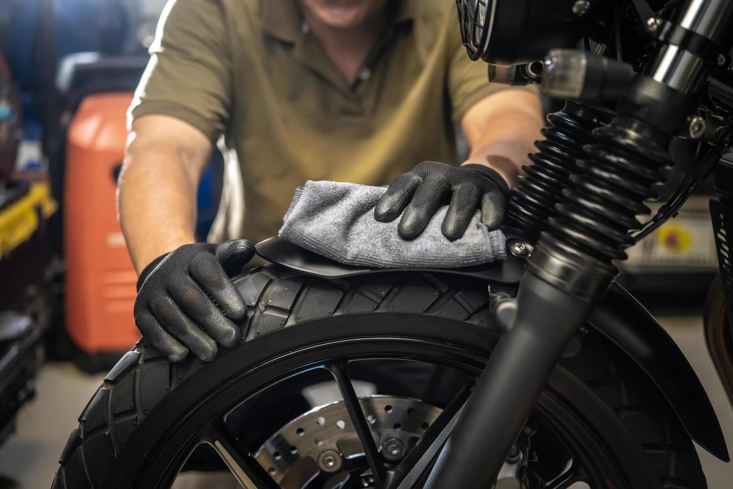 biker man die motorfiets schoonmaakt, gepolijst en wax spray op het voorspatbord bedekt. reparatie en onderhoud motorfiets concept. foto