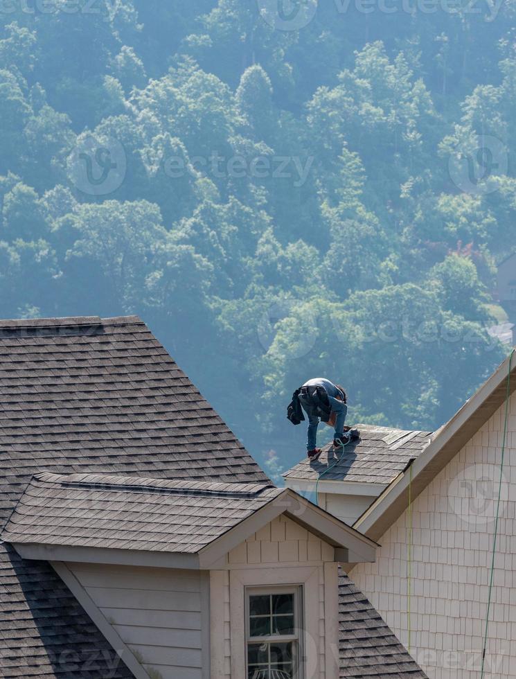 jonge dakdekker die dakspanen spijkert op een dak hoog boven de grond foto