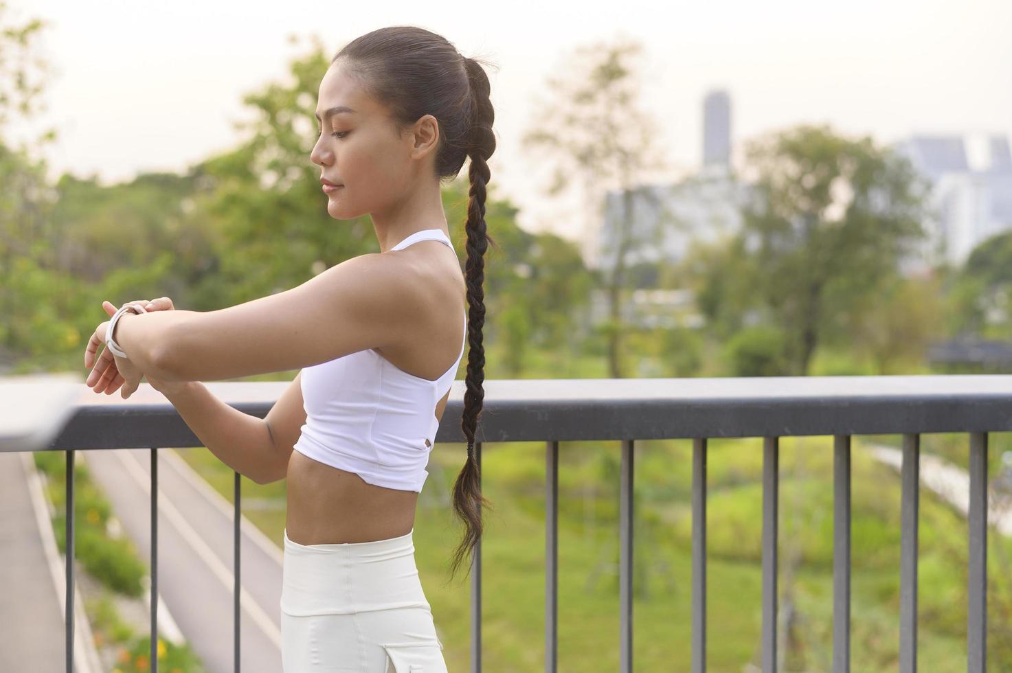 een jonge fitnessvrouw in sportkleding die een slim horloge gebruikt tijdens het sporten in het stadspark, gezond en levensstijl. foto