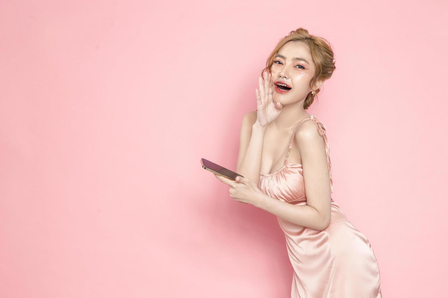 portret vrolijke mooie jonge Aziatische vrouw opgewonden met smartphone in haar hand op roze achtergrond. geweldig mobiel aanbod, consumentisme, lifestyle concept. foto