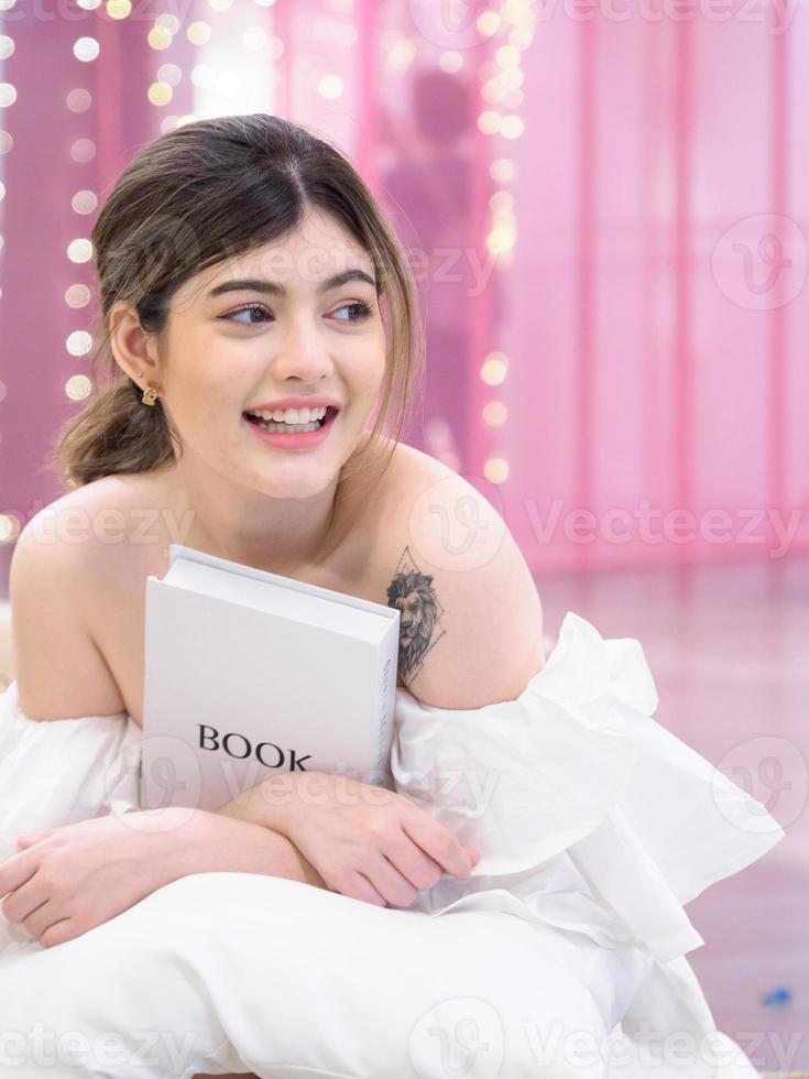 portret jong mooi meisje vrouw vrij lachend zitten aantrekkelijk kijken naar boek met een glimlach, gelukkig en helder genieten in slaapzaal universiteit in huiskamer. foto