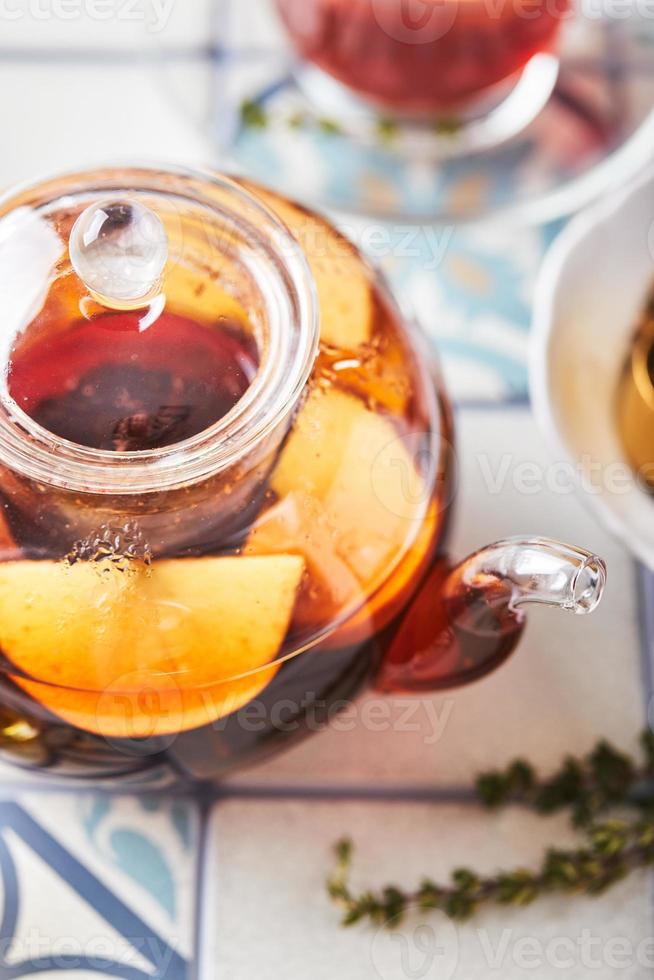 fruit thee met appels en tijm in glas theepot en kop Aan tafel gemaakt van gekleurde tegels foto