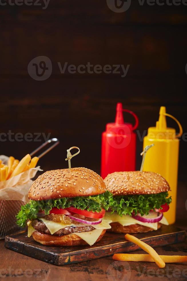 twee eigengemaakt hamburgers met rundvlees, kaas en ui marmelade Aan een houten bord, Patat in een metaal mand en sauzen. snel voedsel concept, Amerikaans voedsel foto