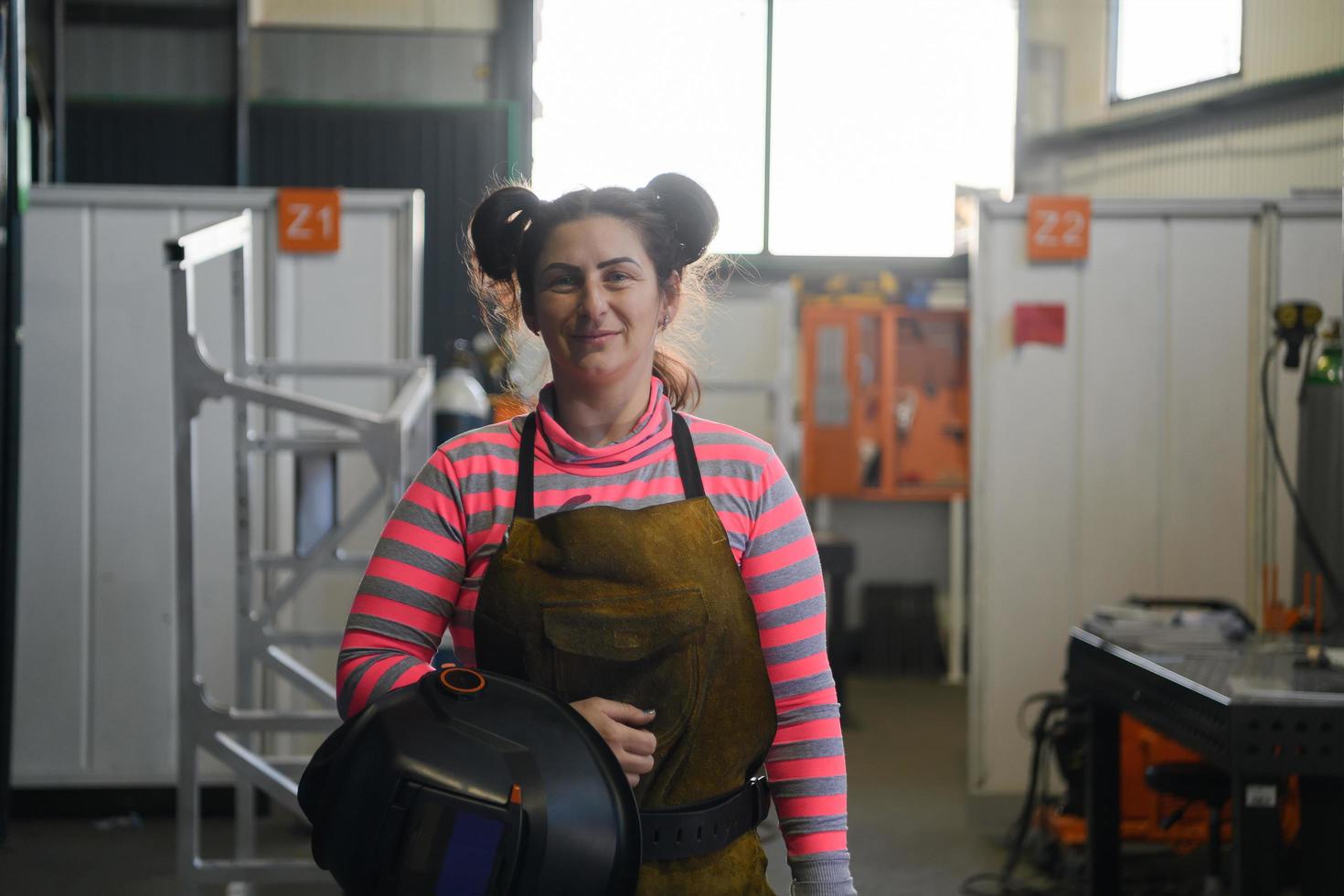 een portret van een Dames lasser Holding een helm en voorbereidingen treffen voor een werken dag in de metaal industrie foto