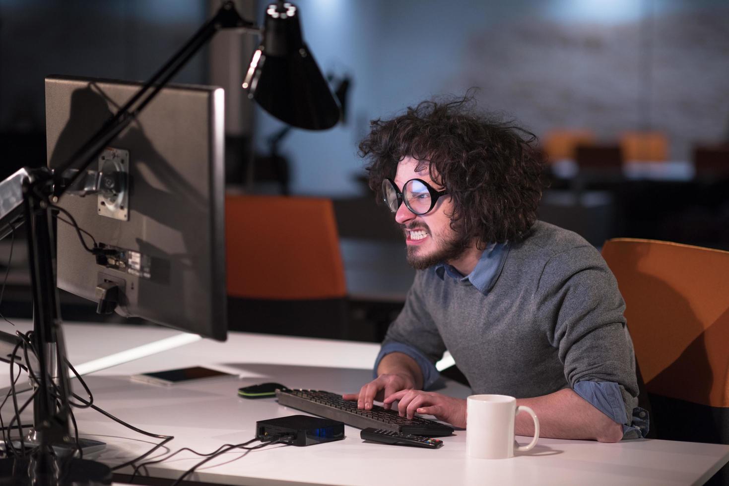 Mens werken Aan computer in donker opstarten kantoor foto