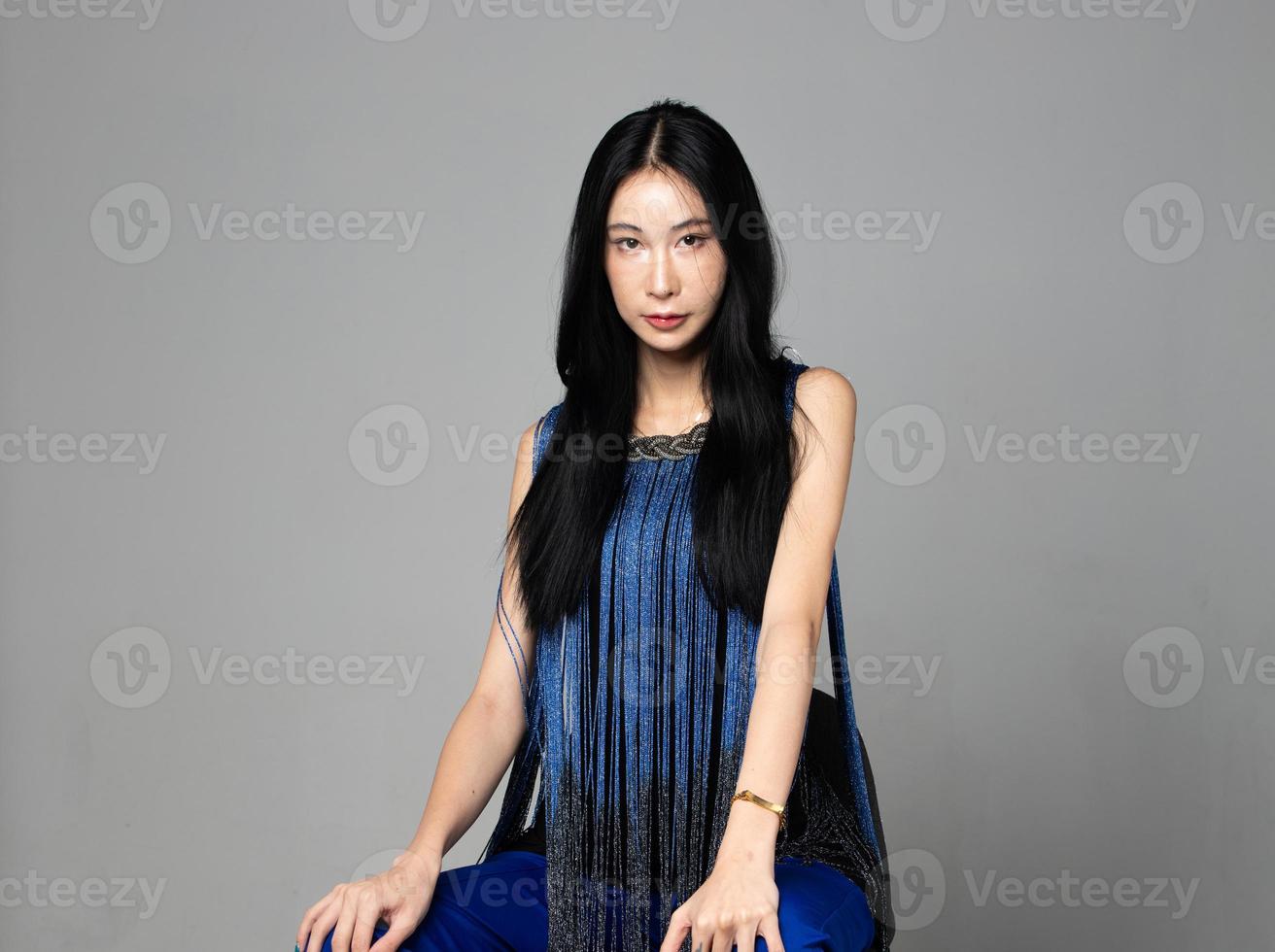 Aziatisch transgender vrouw met lang zwart Rechtdoor haar, kijken Bij camera. vrouw zitten en slijtage blauw mode sensueel sexy jurk, grijs achtergrond geïsoleerd kopiëren ruimte foto
