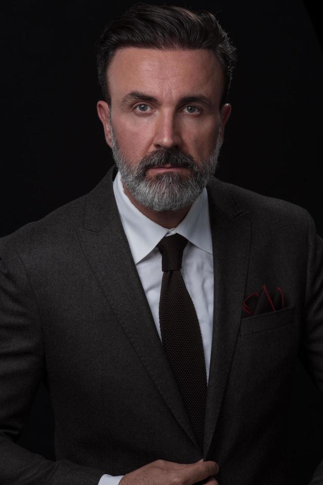 portret van een elegant elegant senior zakenman met een baard en gewoontjes bedrijf kleren in foto studio geïsoleerd Aan donker achtergrond gebaren met handen