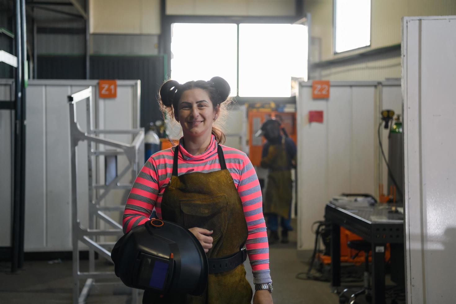 een portret van een Dames lasser Holding een helm en voorbereidingen treffen voor een werken dag in de metaal industrie foto