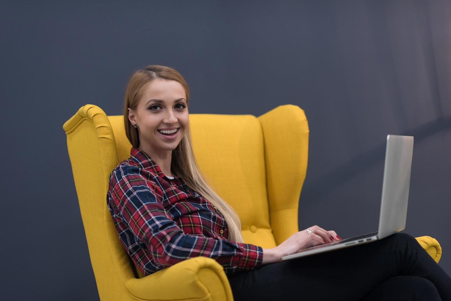 opstarten bedrijf, vrouw werken Aan laptop en zittend Aan geel fauteuil foto