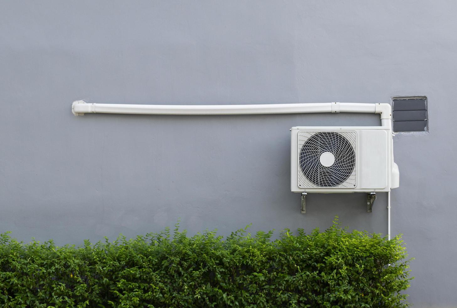 lucht compressor Aan grijs muur met groen struik foto