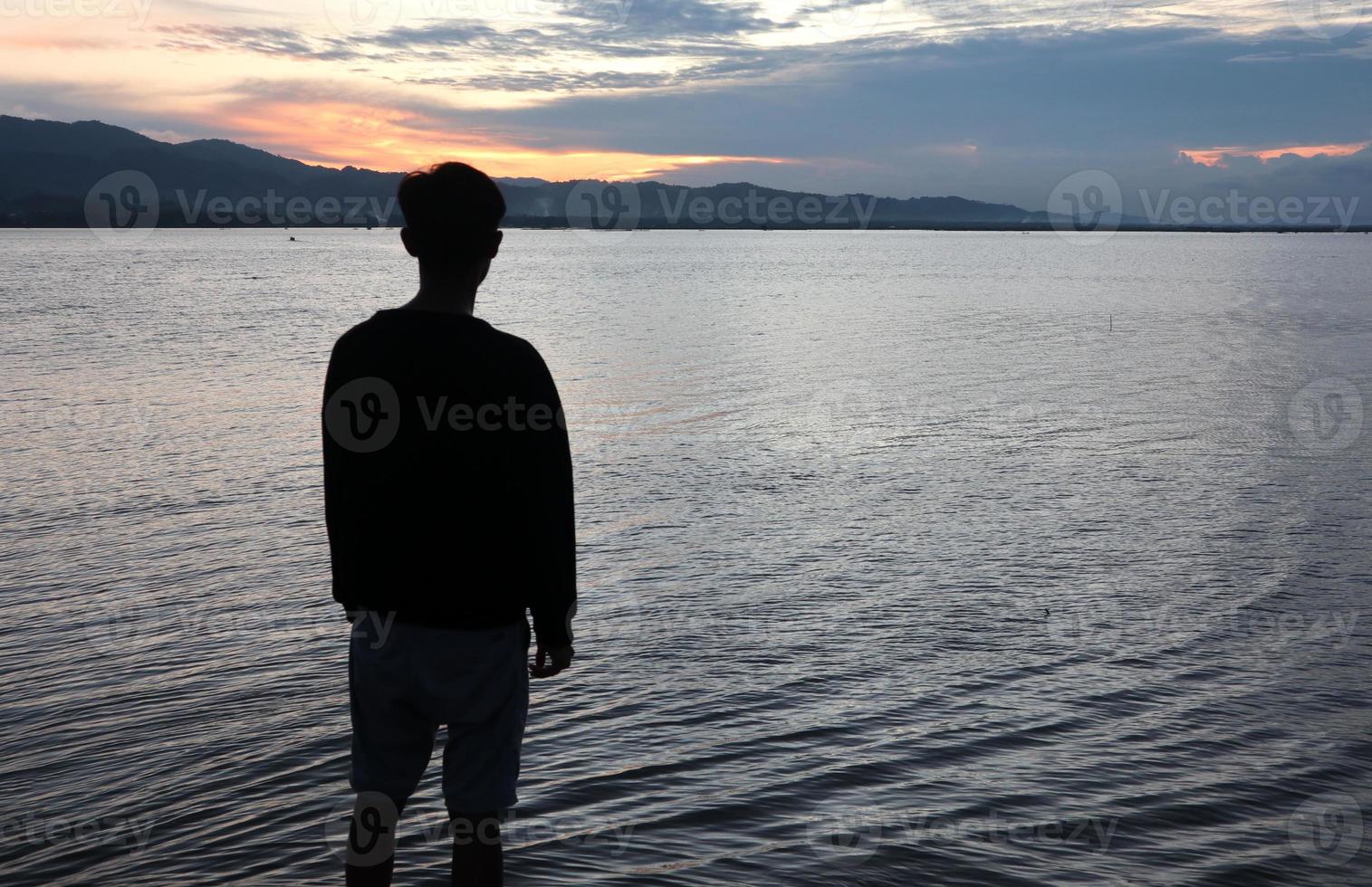 silhouet van een jong Mens staand door de meer genieten van de zonsondergang. vredig atmosfeer in natuur foto