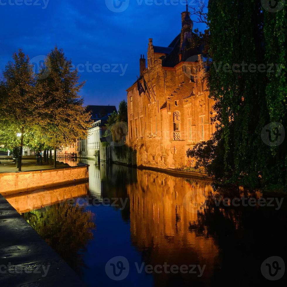 oud middeleeuws steen Europa huis weerspiegeld Aan de water van grachten visie in Brugge, belgië. nacht tafereel met verlichting en reflecties foto