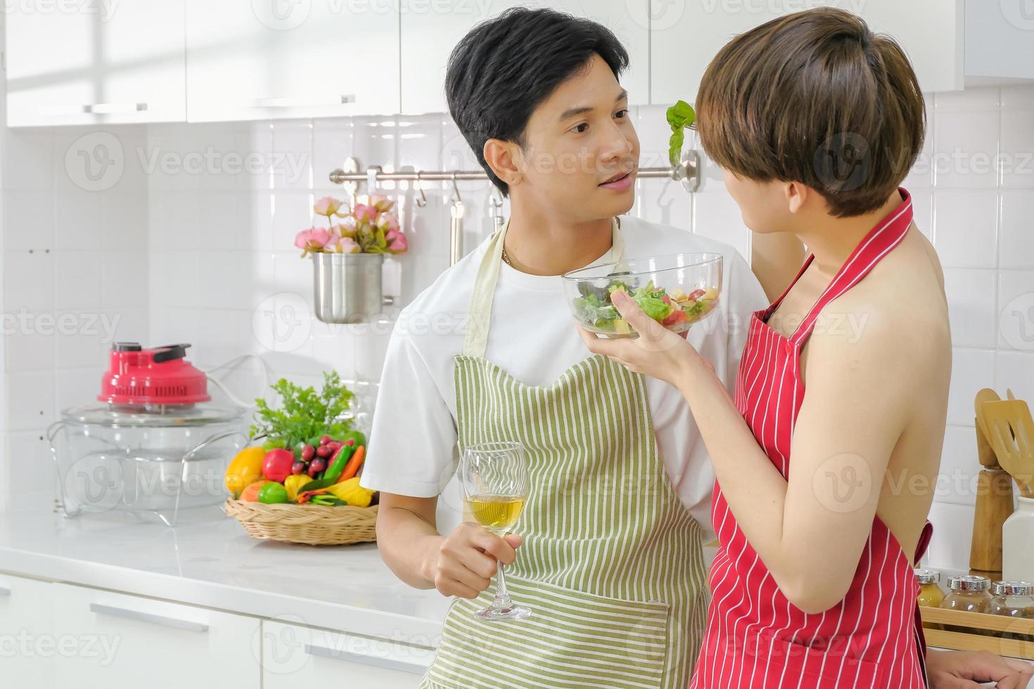 jong lgbt paar huiselijk leven concept. intiem Aziatisch jong lgbt mannetje paar genieten aan het eten salade met wijn glas in hand- en hebben romantisch momenten samen in de keuken Bij huis. selectief focus. foto