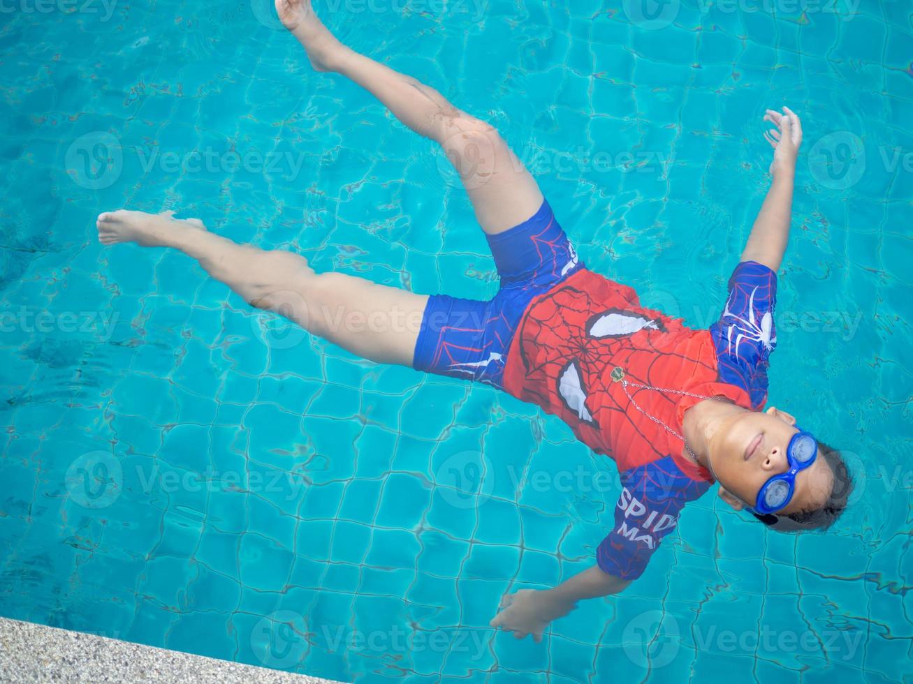 jongen vervelend een zwempak en bril zwemmen in de midden- van de zwembad met een blauw water achtergrond foto