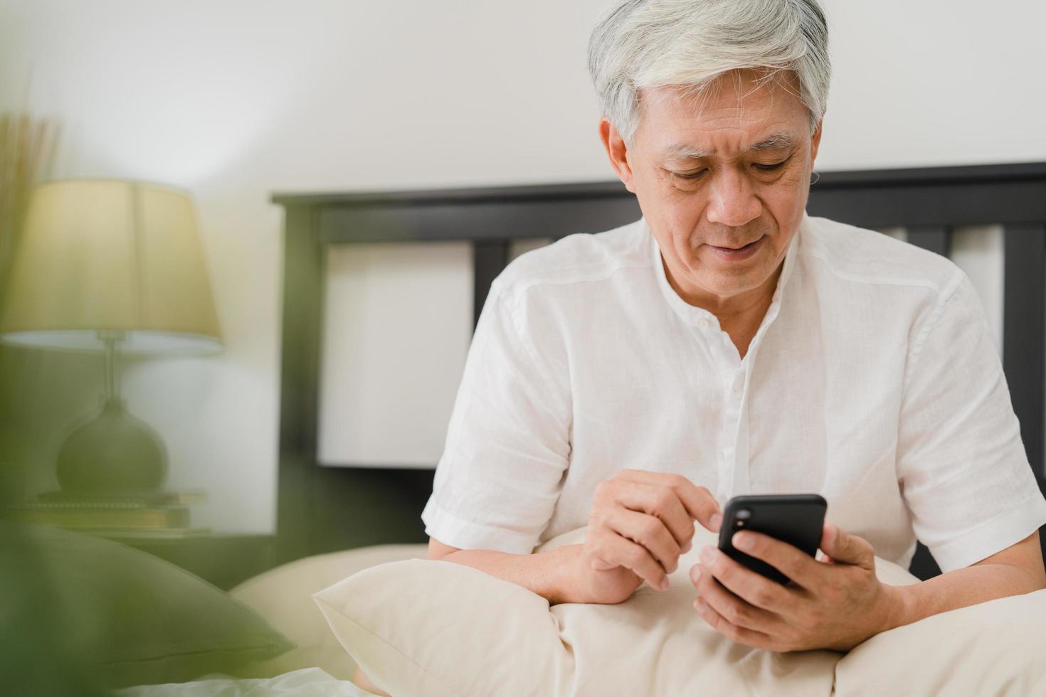 Aziatische senior man met behulp van mobiele telefoon thuis foto