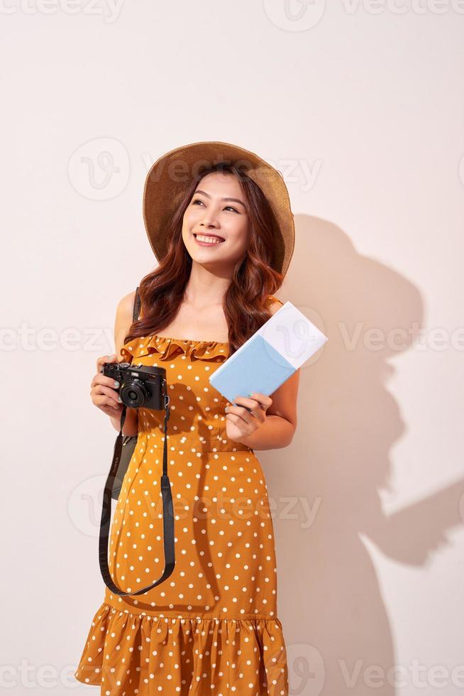 portret van een gelukkig jong vrouw in hoed Holding camera en tonen paspoort terwijl staand geïsoleerd over- beige achtergrond foto