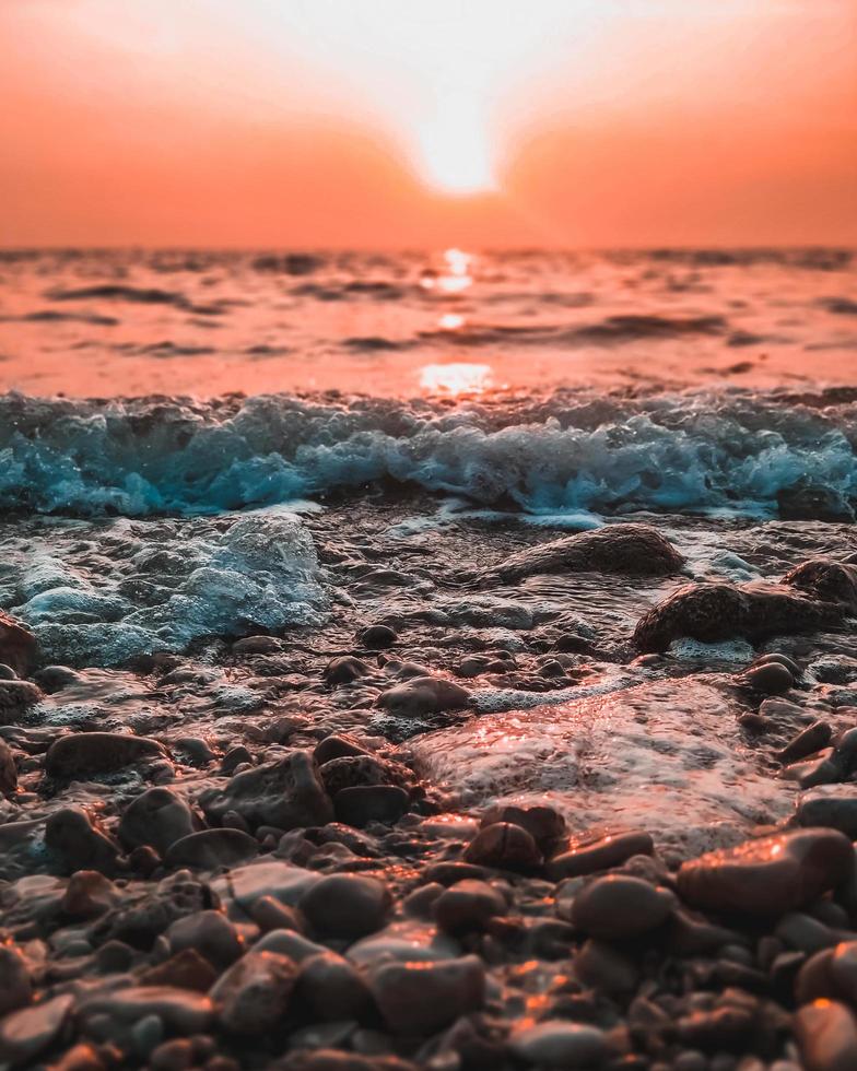 stenen en golven op het strand met kleurrijke hemel foto