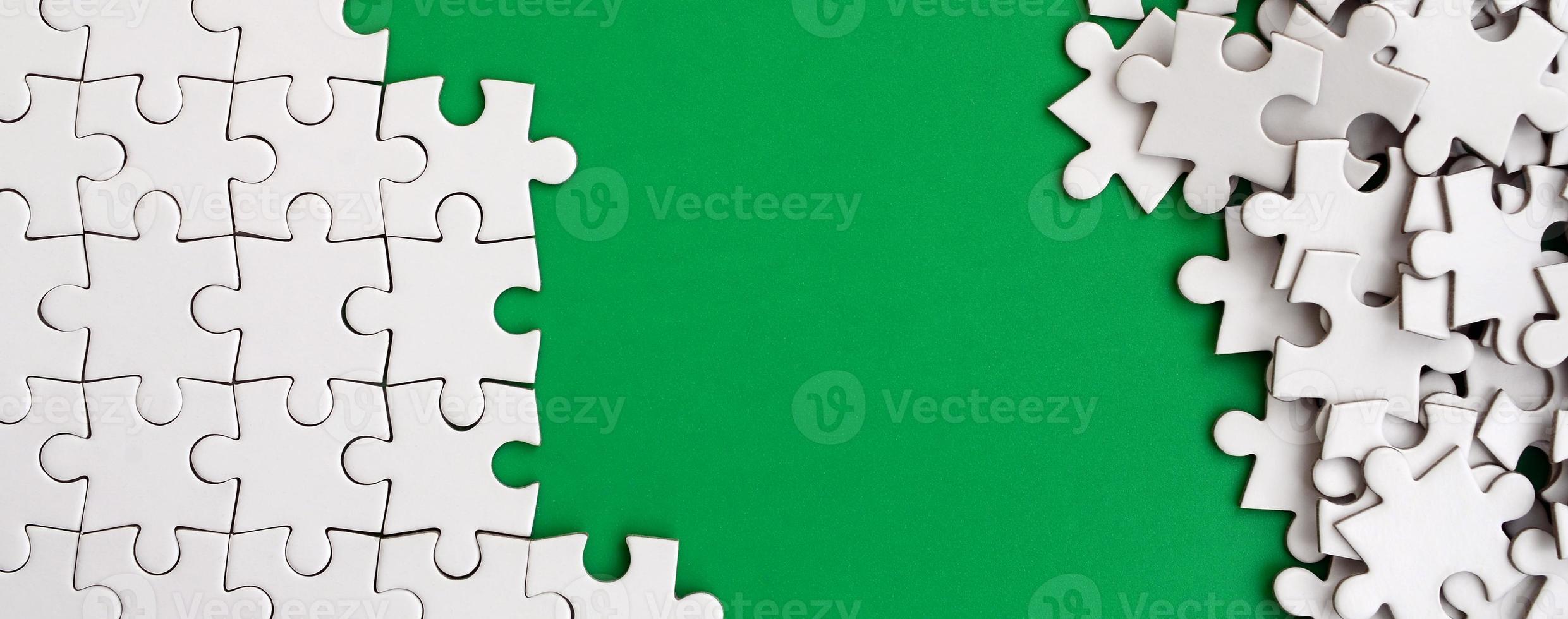 fragment van een gevouwen wit decoupeerzaag puzzel en een stapel van ongekamd puzzel elementen tegen de achtergrond van een groen oppervlak. structuur foto met ruimte voor tekst