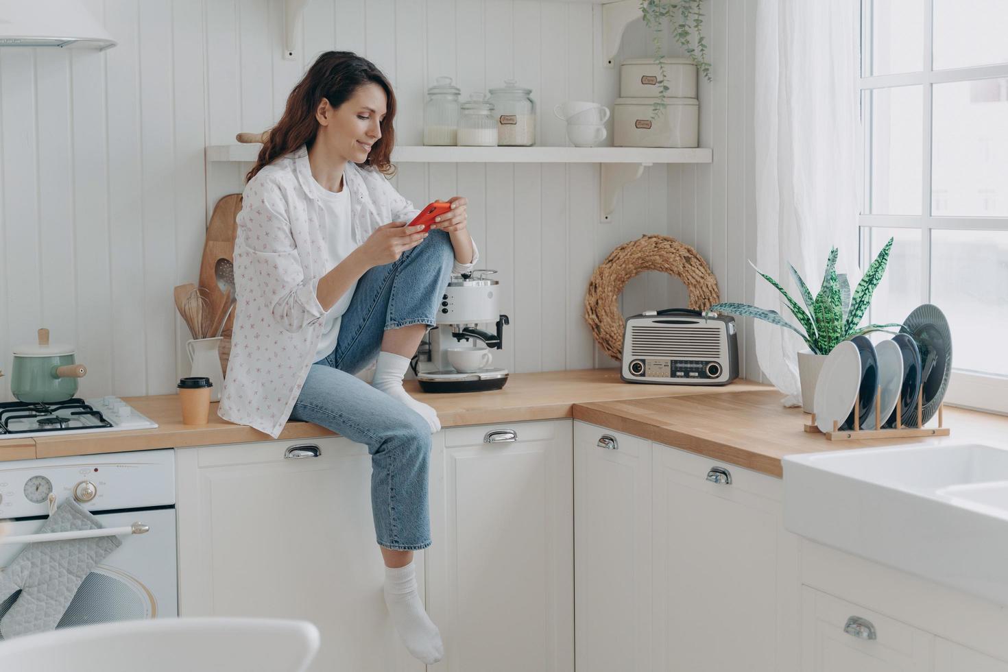 vrouw boodschappen doen boodschappen online door mobiel telefoon app, zittend in modern keuken Bij huis. e handel foto