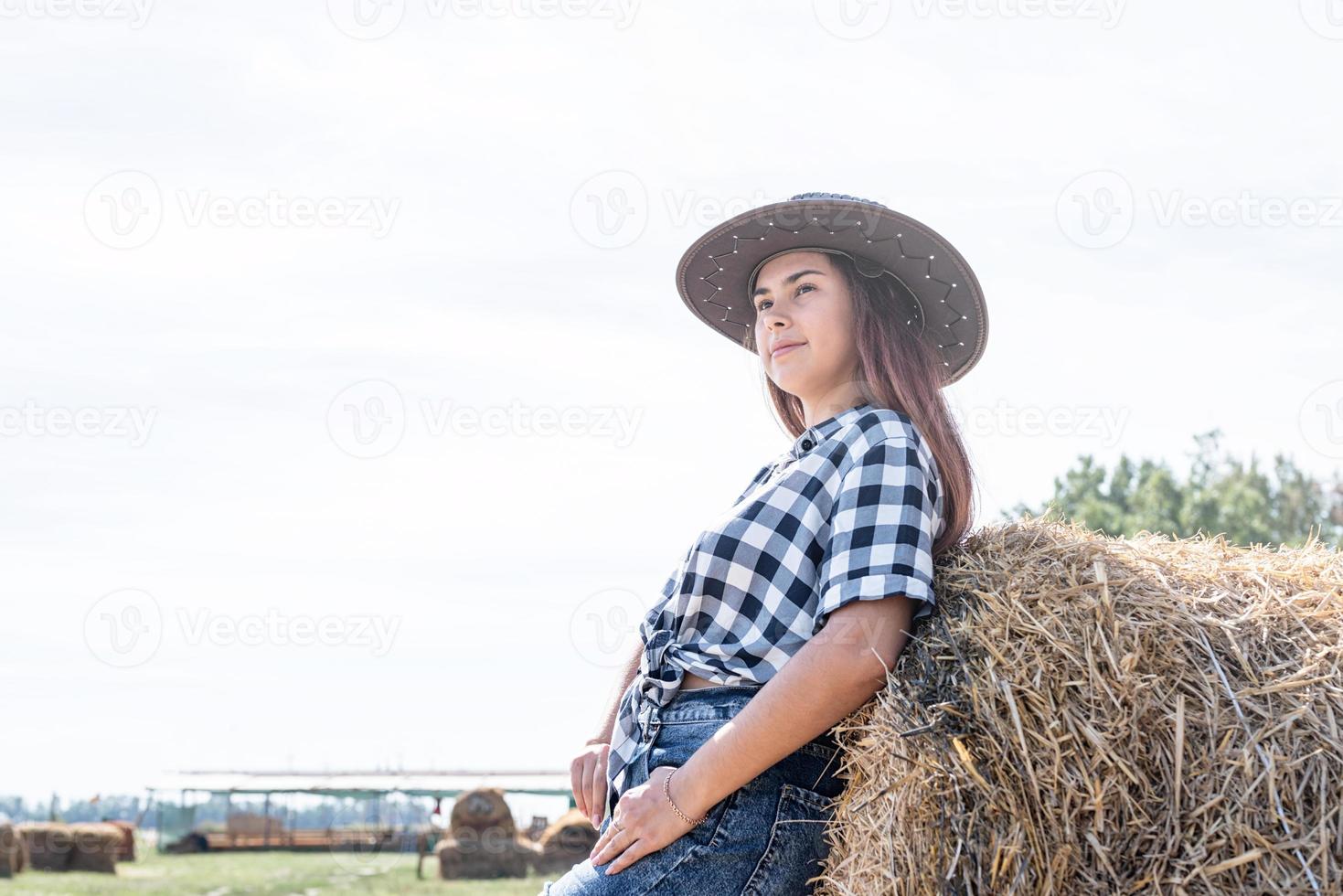 mooi vrouw in plaid overhemd en cowboy hoed resting Aan hooiberg foto