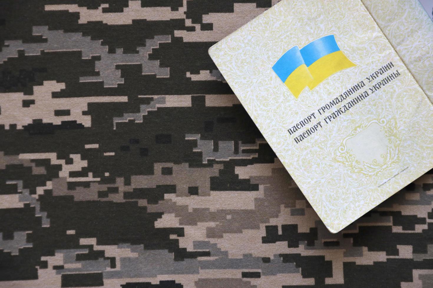 sumie, Oekraïne - maart 20, 2022 oekraïens buitenlands paspoort Aan kleding stof met structuur van leger korrelig camouflage. kleding met camo patroon in grijs, bruin en groen pixel vormen en oekraïens ID kaart foto