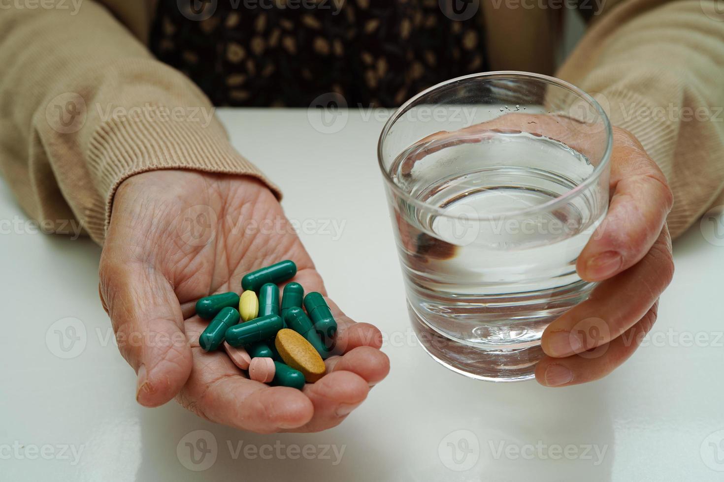 Aziatische bejaarde vrouw met pil drug met water in glas, sterk gezond medisch concept. foto