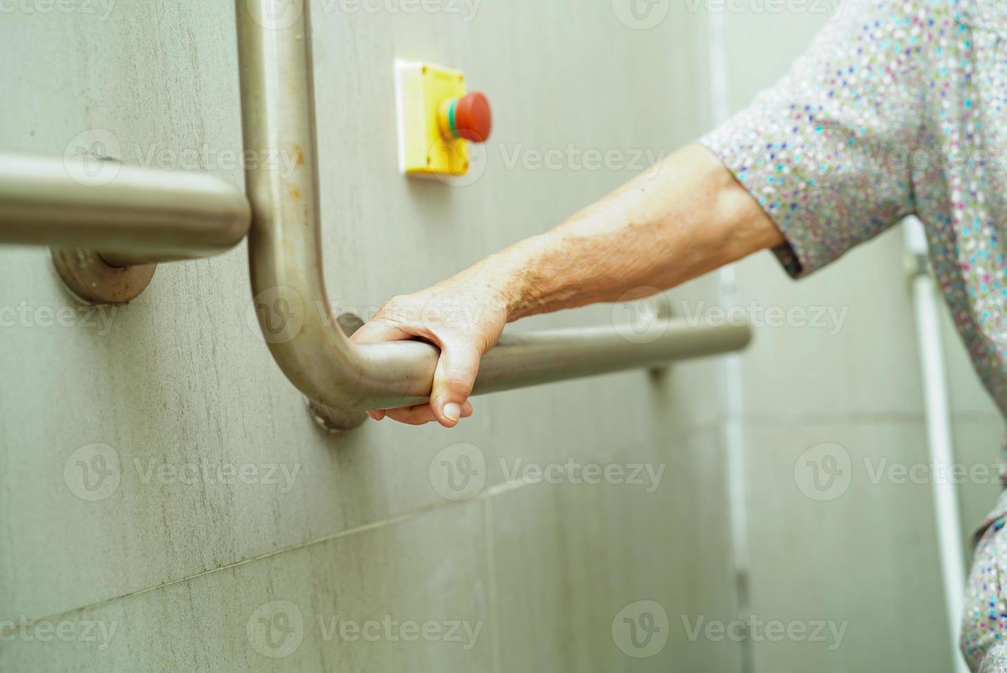 Aziatische bejaarde oude vrouw patiënt gebruik toilet steunrail in badkamer, leuning veiligheid handgreep, beveiliging in verpleegziekenhuis. foto