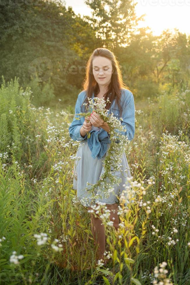 mooi meisje lopen op veld op zomer met wilde bloemen. foto
