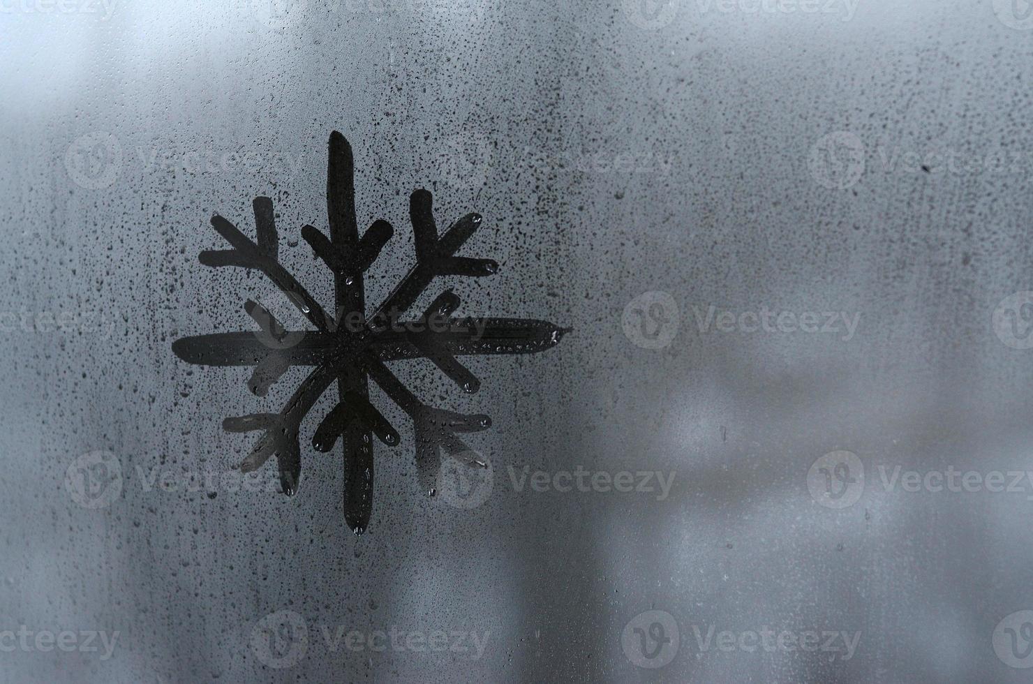 de beeld van de sneeuwvlok is getrokken met een vinger Aan de oppervlakte van een beneveld glas venster. ijzig weer foto