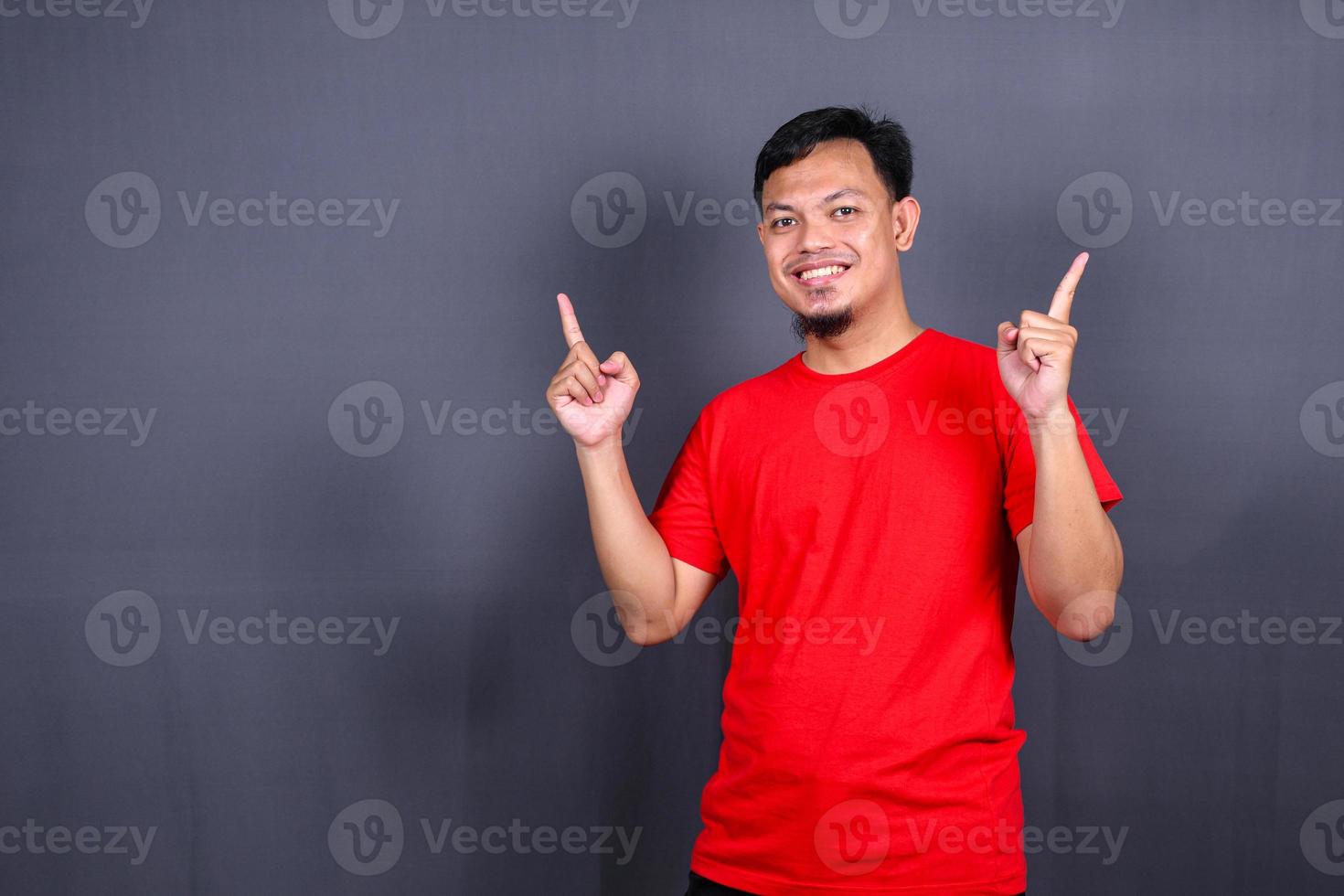 Aziatisch jong Mens in rood t-shirt richten met zijn vinger geïsoleerd Aan grijs achtergrond foto