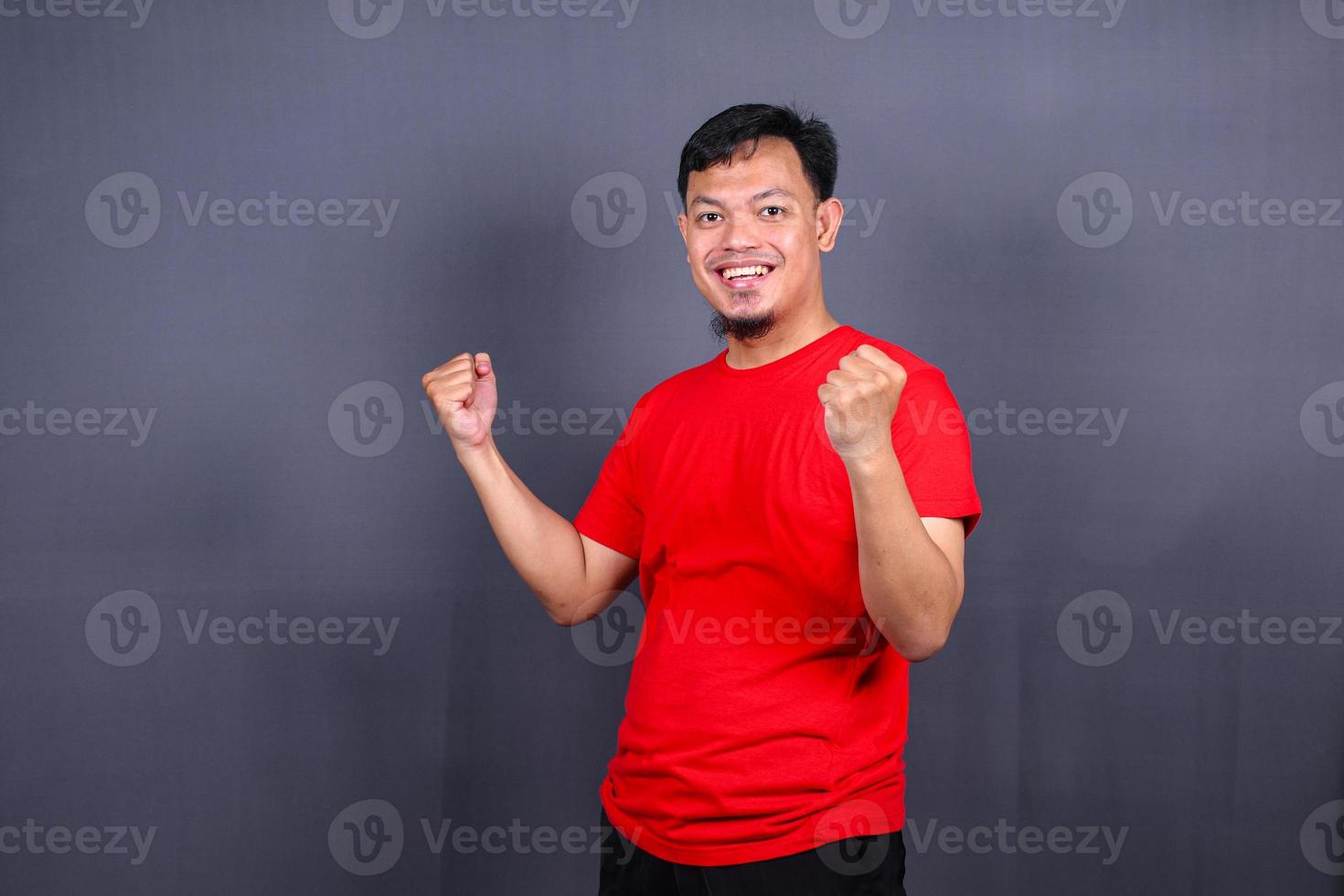 portret van een opgewonden Aziatisch Mens staand met verheven handen en op zoek Bij camera geïsoleerd Aan grijs achtergrond vieren succes, zege. foto