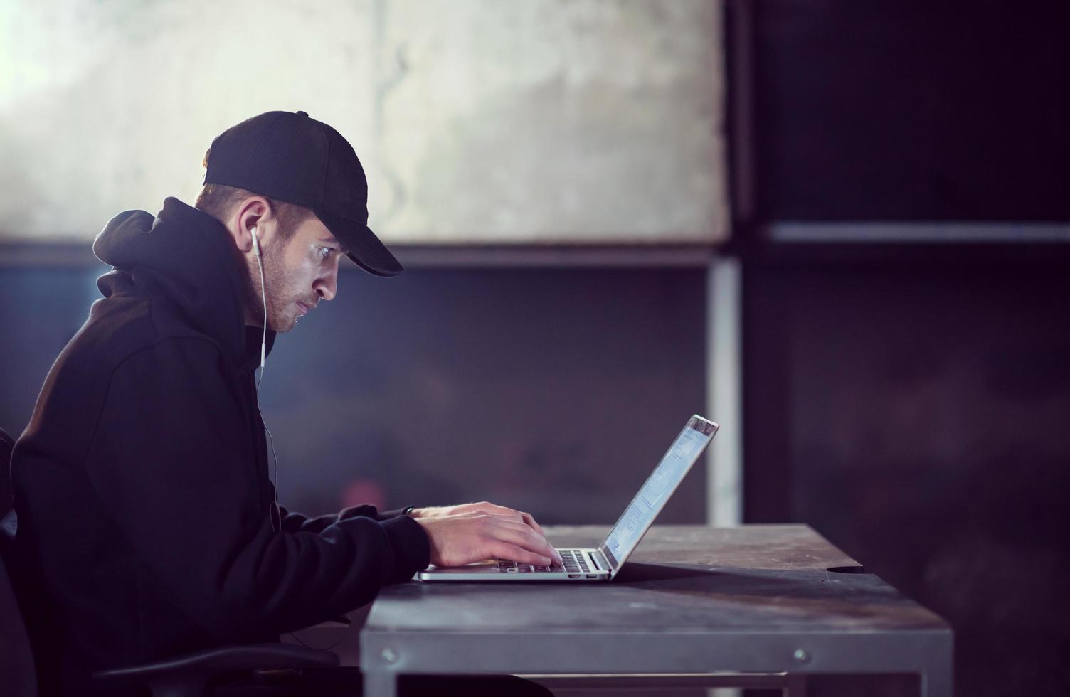 getalenteerd hacker gebruik makend van laptop computer terwijl werken in donker kantoor foto