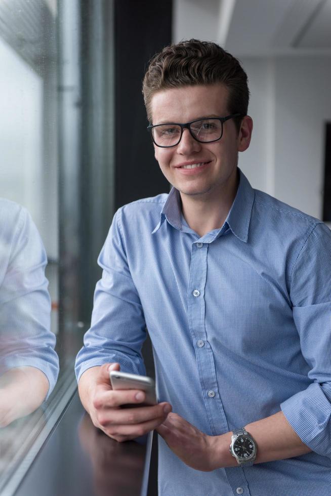 zakenman staand in een modern gebouw in de buurt de venster met telefoon foto