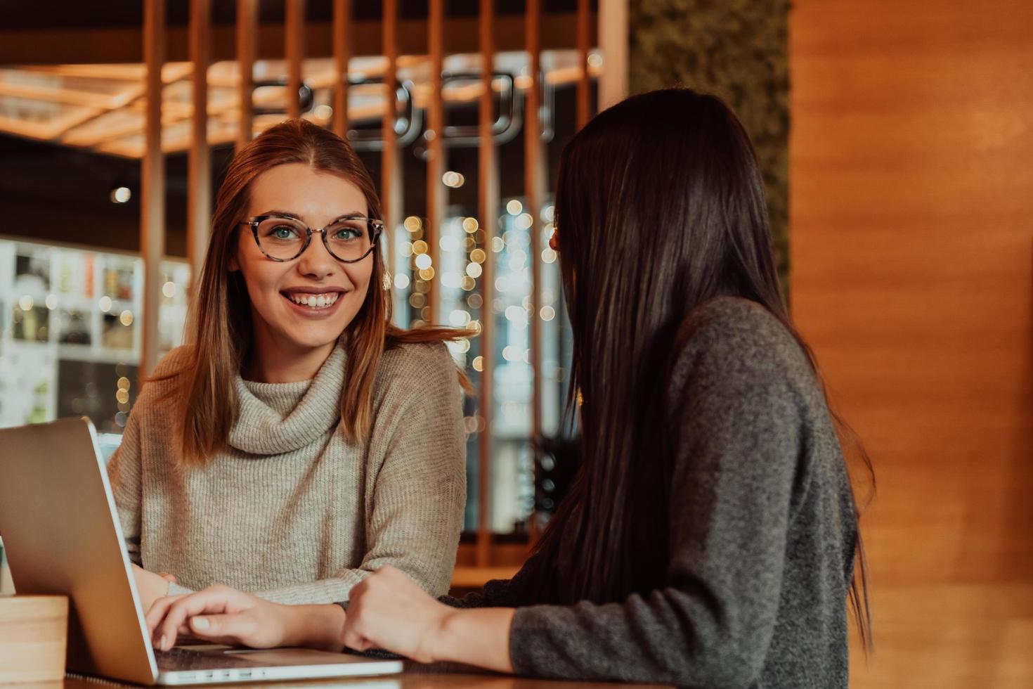 twee jong bedrijf Dames zittend Bij tafel in cafe. meisje shows collega informatie Aan laptop scherm. meisje gebruik makend van smartphone, bloggen. teamwerk, bedrijf ontmoeting. foto