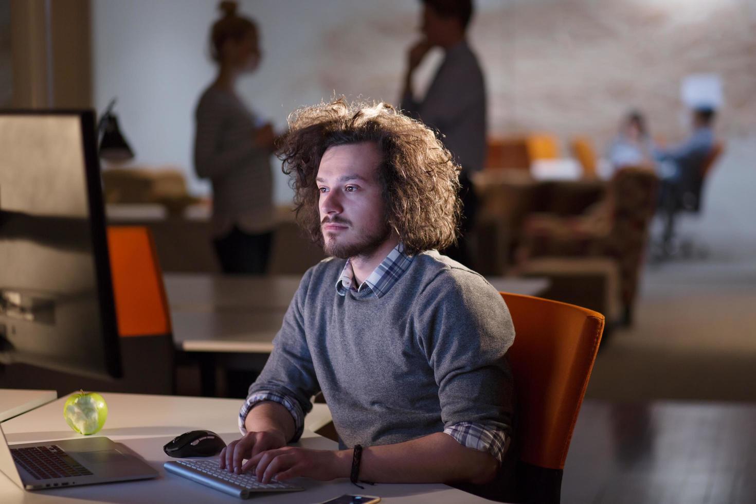 Mens werken Aan computer in donker kantoor foto