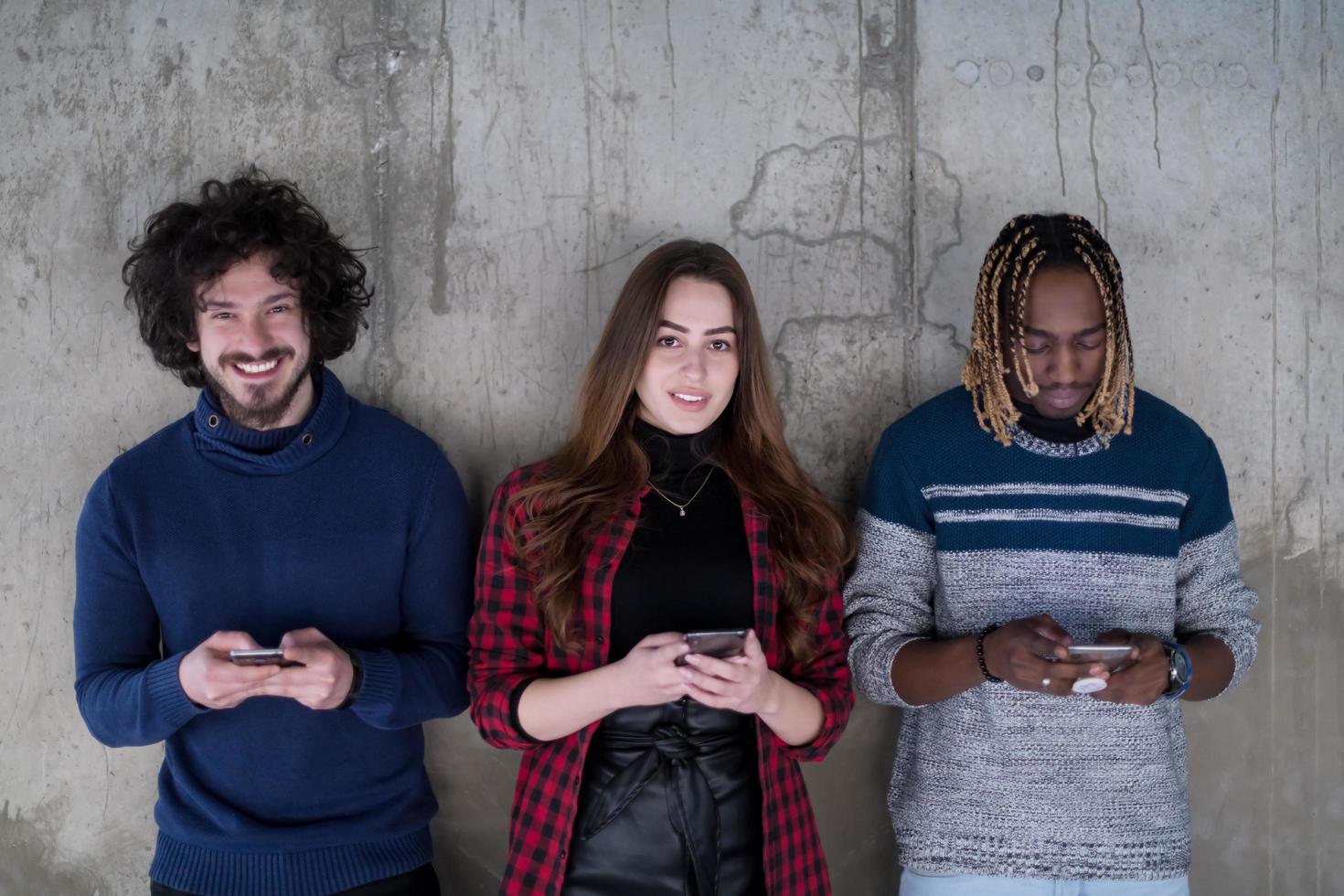 gewoontjes multi-etnisch bedrijf team gebruik makend van mobiel telefoons in voorkant van een beton muur foto