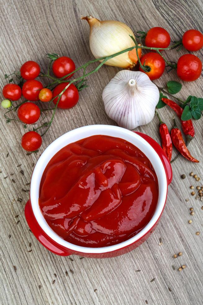 tomaat ketchup in een kom Aan houten achtergrond foto
