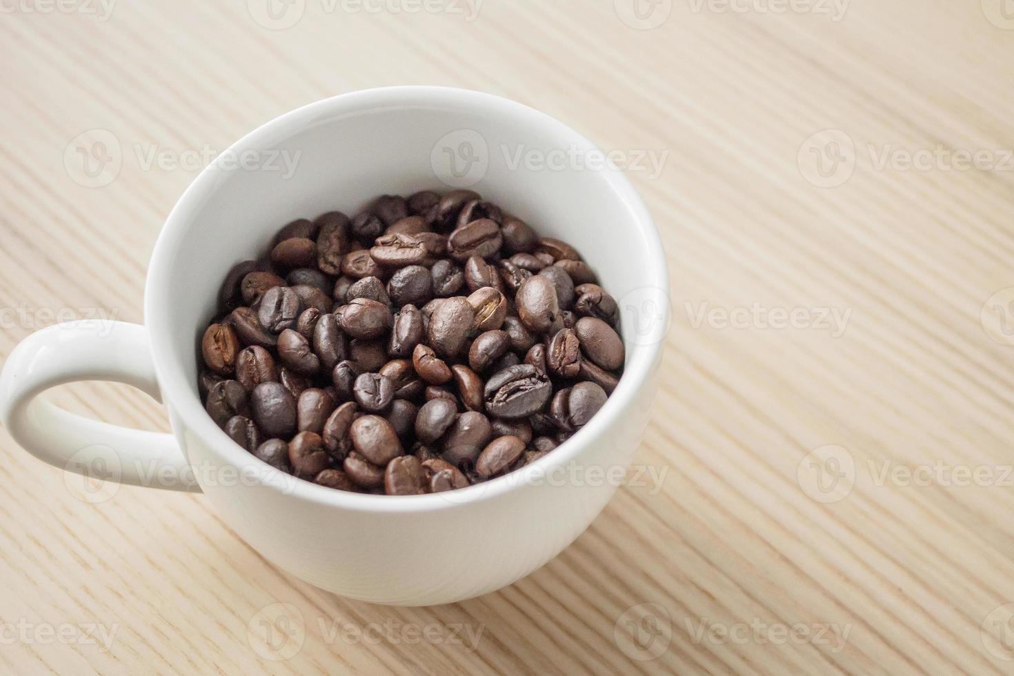 vers geroosterd koffie bonen in wit kop Aan hout tafel foto