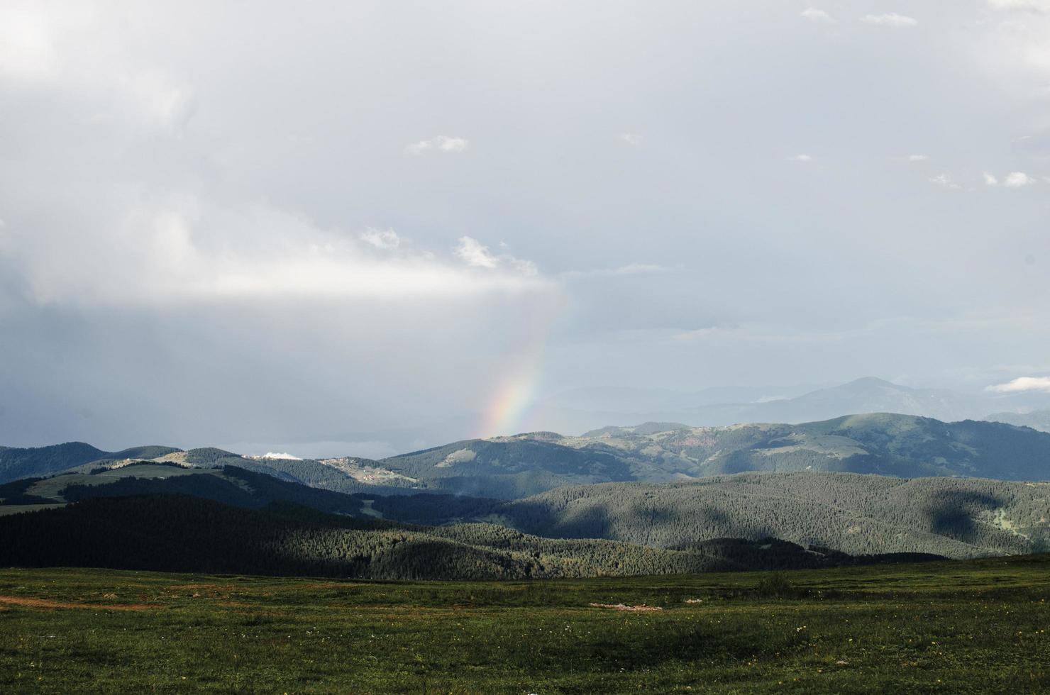 grasveld met bergen en een regenboog in de verte foto