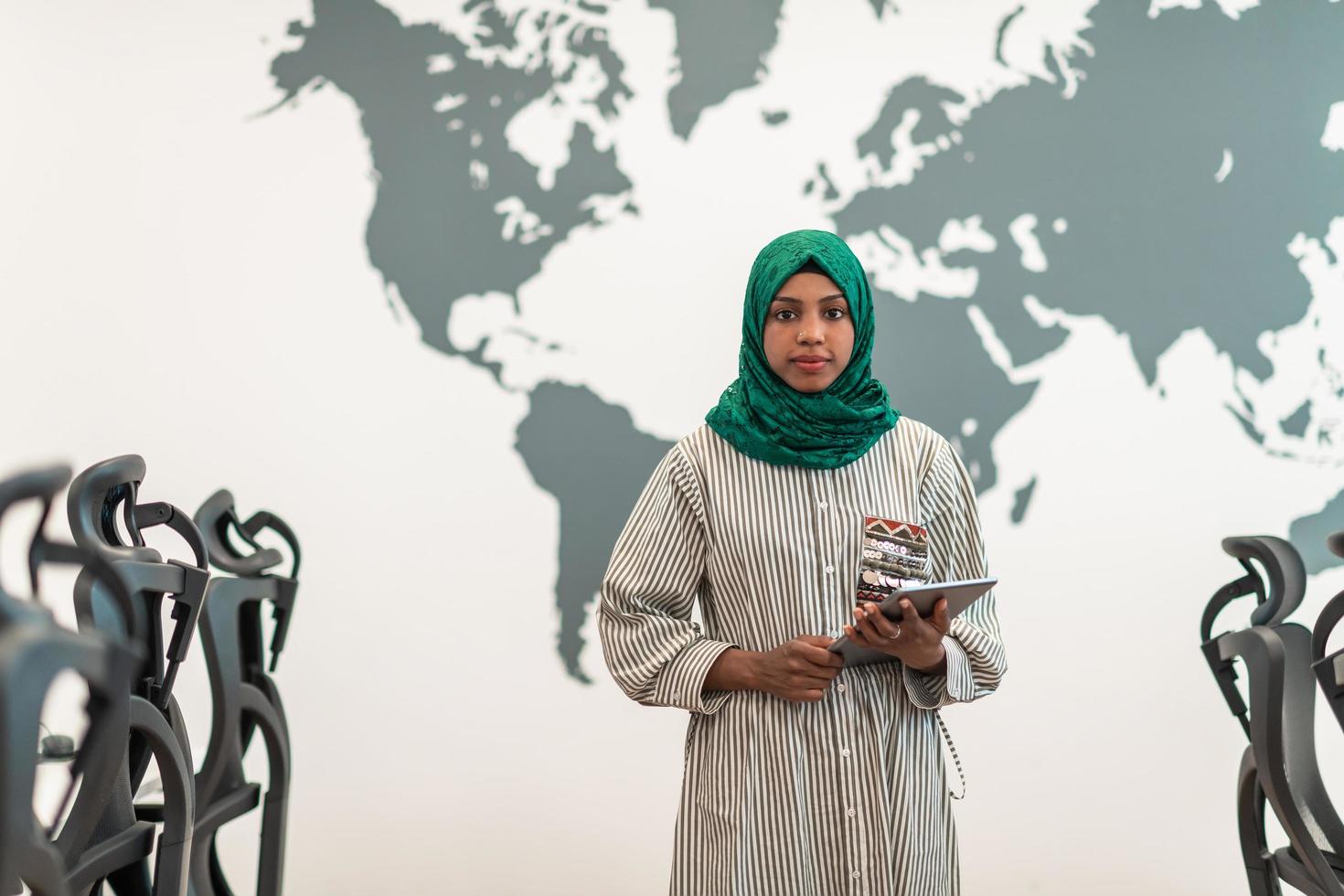 portret van moslim vrouw software ontwikkelaar met groen hijab Holding tablet computer terwijl staand Bij modern Open plan opstarten kantoor foto