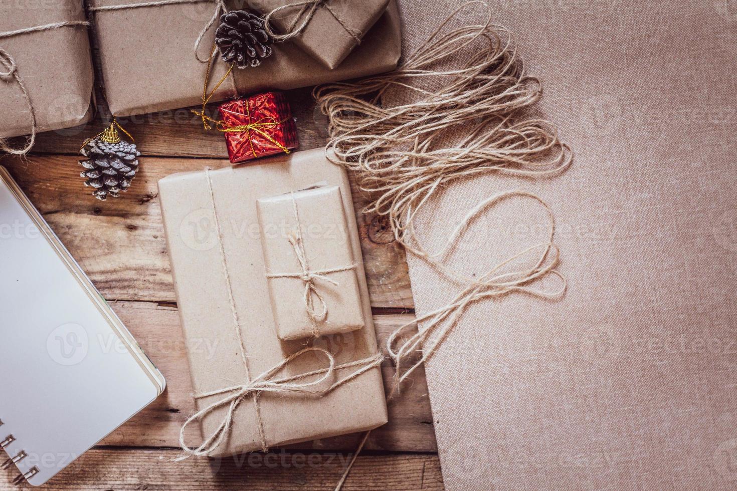 Kerstmis geschenk doos gebruik bruin gerecycled papier en een notitieboekje en pijnboom kegels Aan een houten tafel. foto