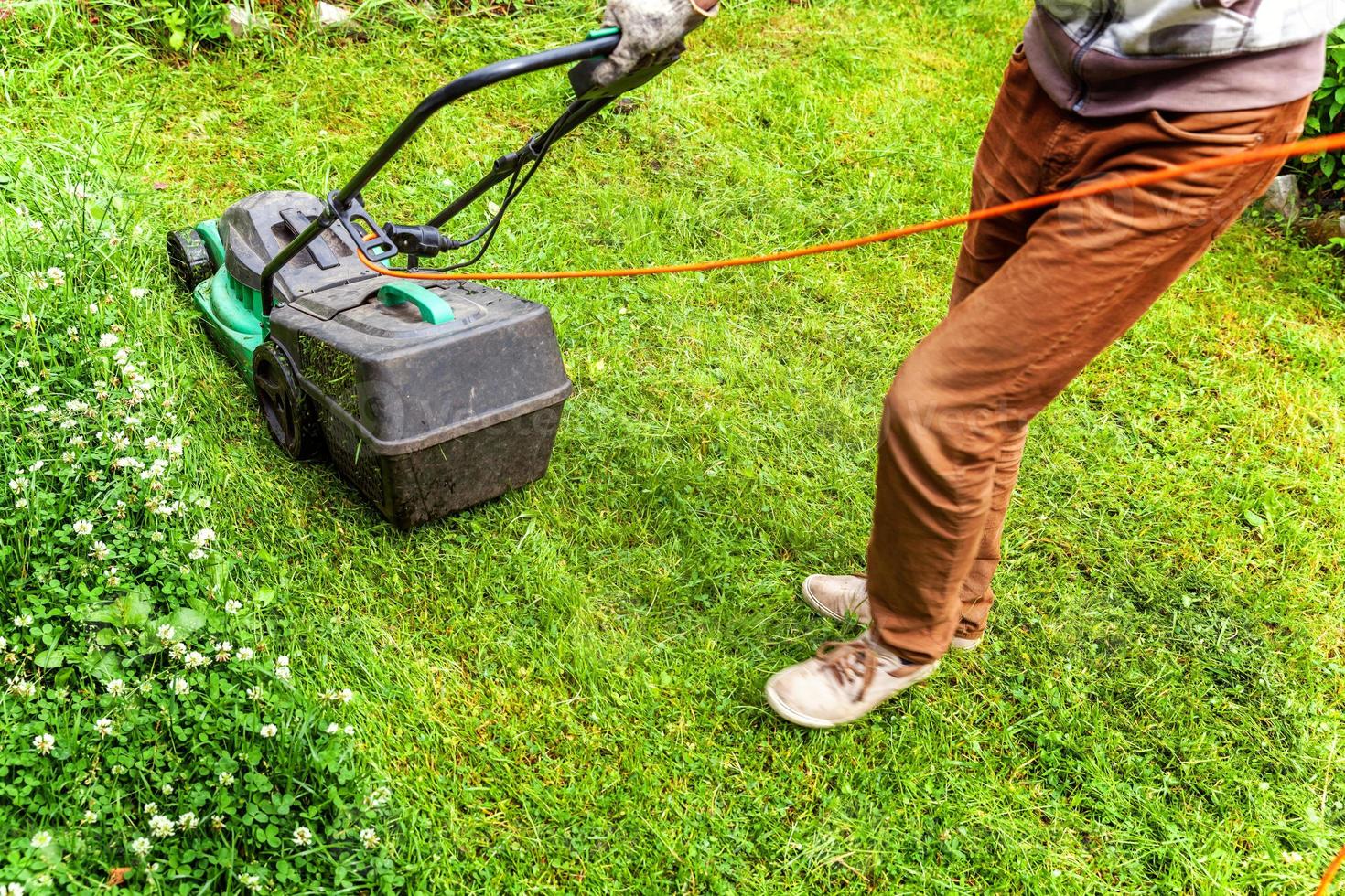 man die groen gras snijdt met grasmaaier in de achtertuin. tuinieren land levensstijl achtergrond. prachtig uitzicht op vers groen grasgazon in zonlicht, tuinlandschap in lente- of zomerseizoen. foto