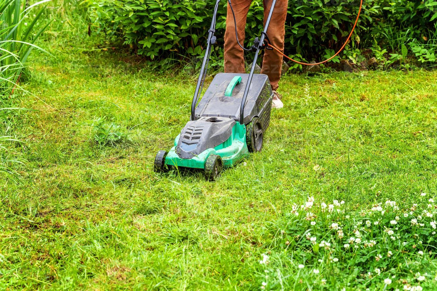 man die groen gras snijdt met grasmaaier in de achtertuin. tuinieren land levensstijl achtergrond. prachtig uitzicht op vers groen grasgazon in zonlicht, tuinlandschap in lente- of zomerseizoen. foto