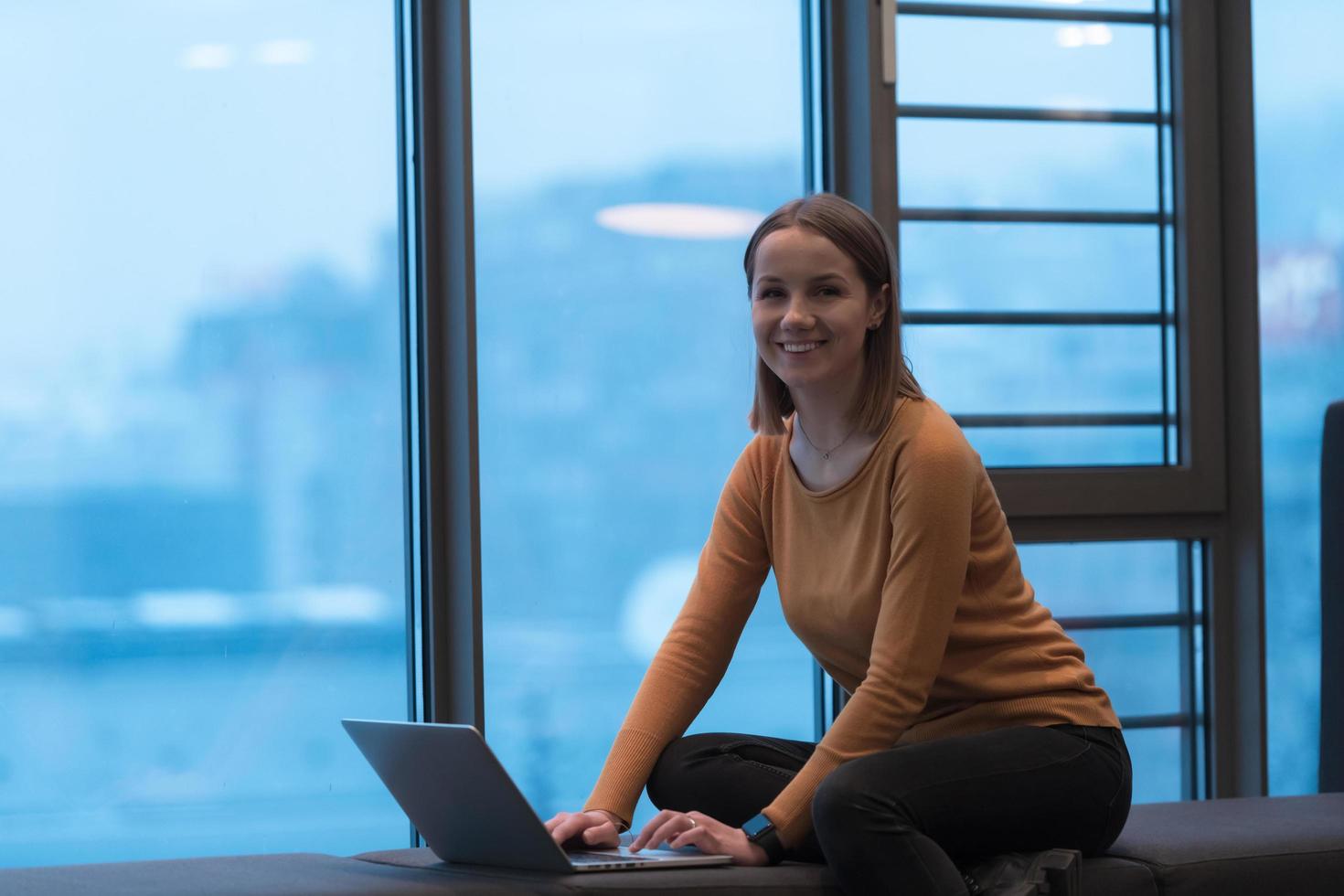 een jong vrouw zittend in een modern ruimte terwijl werken Aan een project Aan een laptop. selectief focus foto