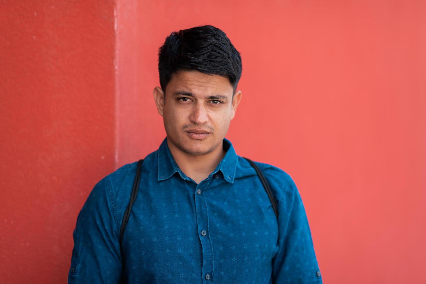 opstarten bedrijf portret van gewoontjes zakenman met een blauw overhemd en rugzak in voorkant van rood muur foto